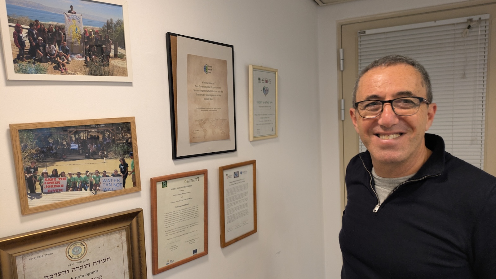 a man in glasses standing next to a wall of documents
