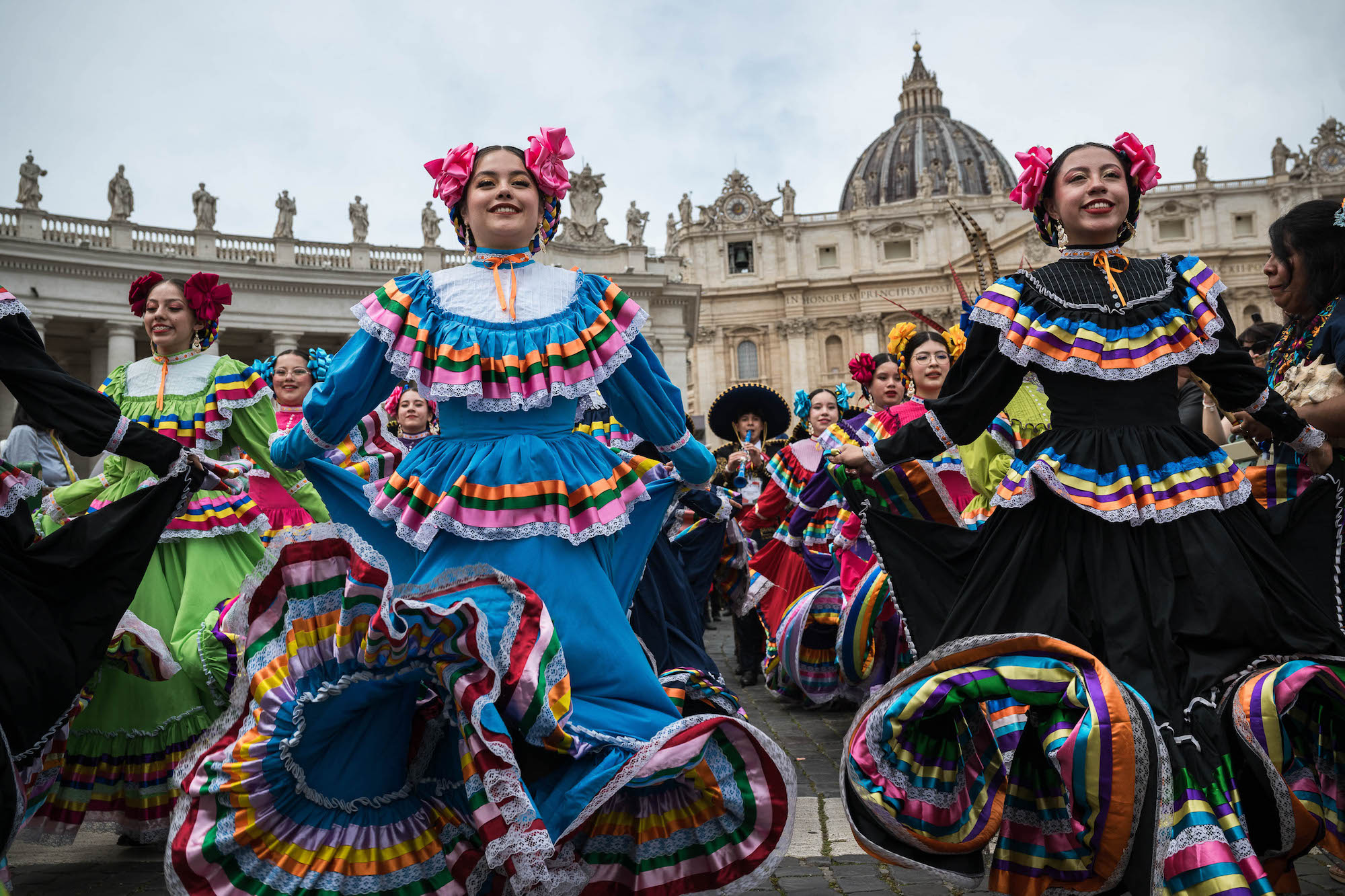 dancers in colorful dresses with ruffles and ribbons dance in front of St. Peter's basilica
