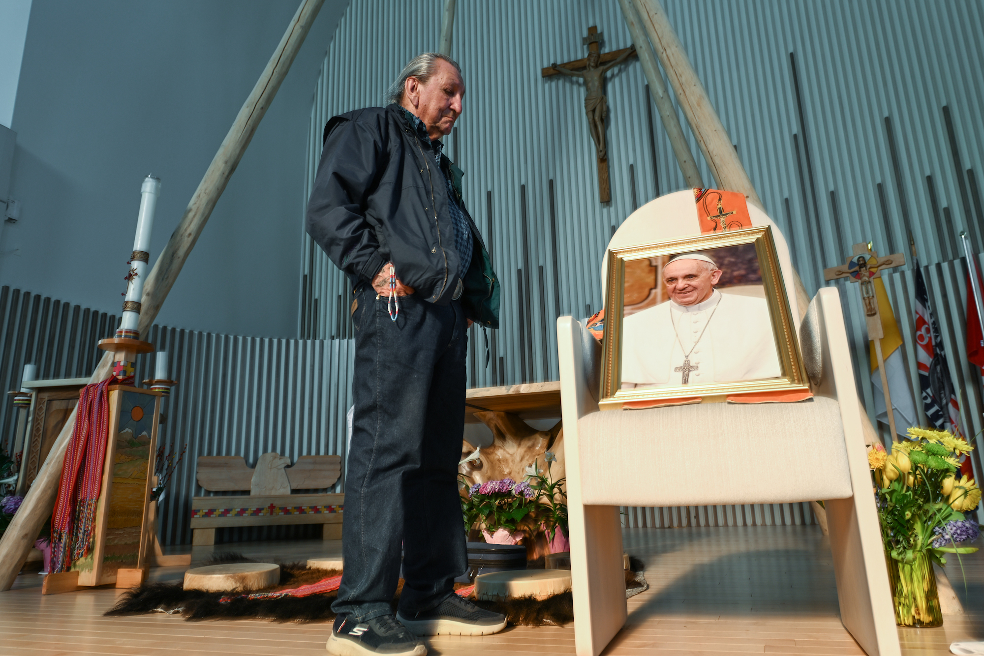 a man in a suit stands next to a chair with a portrait of pope francis